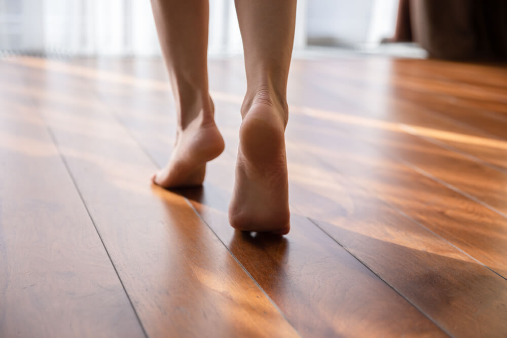 Woman Walking Barefoot on Toes at Warm Laminate Floor Close Up Rear View.