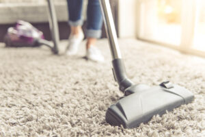 A woman using a vacuum cleaner while cleaning carpet in the house